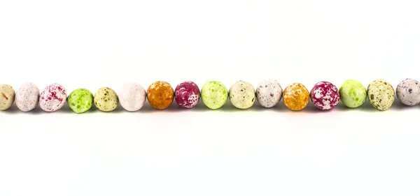 Färgade söta godis jordnötter i glasyr, liknar fågelägg, ligger i rad på en vit bakgrund — Stockfoto