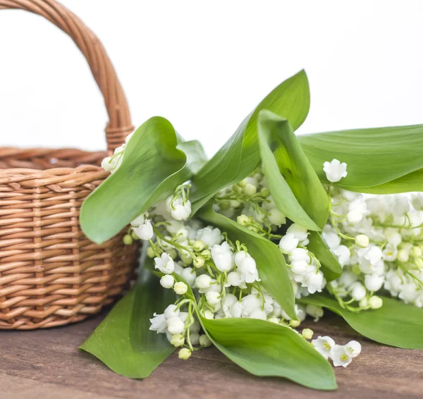 Witte lelies van de vallei met een mand op een houten achtergrond — Stockfoto