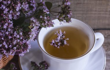 Beyaz bir fincanda kekik çiçekli bitkisel çay, ahşap zemin üzerinde taze kekik çiçekleri..