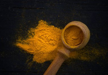 Siyah ahşap arka planda ahşap kaşıklı sarı köri baharatı, yakın plan..