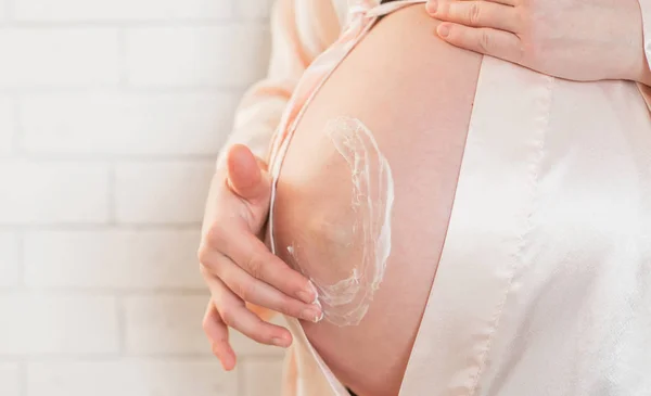 Gravid kvinna att sätta grädde på magen för att undvika bristningar — Stockfoto