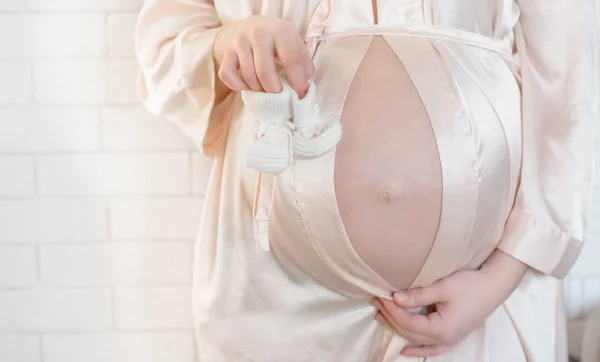 Mulher grávida barriga segurando sapatos de bebê botas — Fotografia de Stock