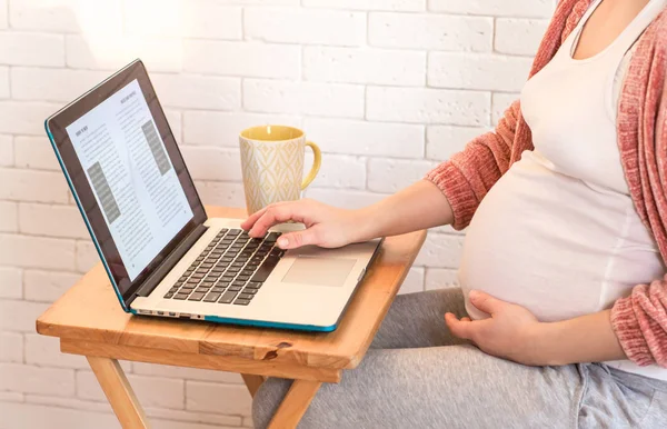 Беременная женщина, работающая с ноутбуком дома — стоковое фото
