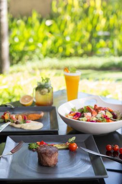 Koyu arka plan üzerinde çeşitli farklı yemekler. Balık, biftek, salata