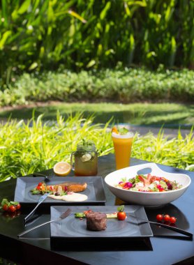 Koyu arka plan üzerinde çeşitli farklı yemekler. Balık, biftek, salata