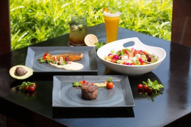 Koyu arka plan üzerinde çeşitli farklı yemekler. Balık, biftek, salata