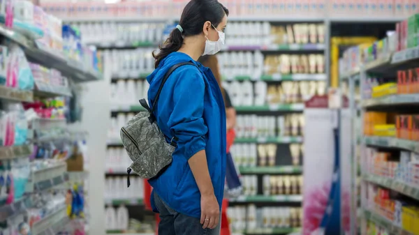 Young woman wears medical mask against coronavirus while shopping in supermarket or store- health, safety and pandemic concept - protective medical mask for protection from virus covid-19