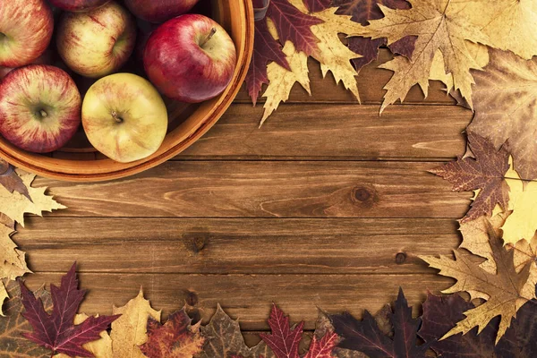 リンゴのバスケットとカエデの葉は木製のテーブルの上に配置されます 平置き 秋の装飾コンセプトのトップビュー — ストック写真