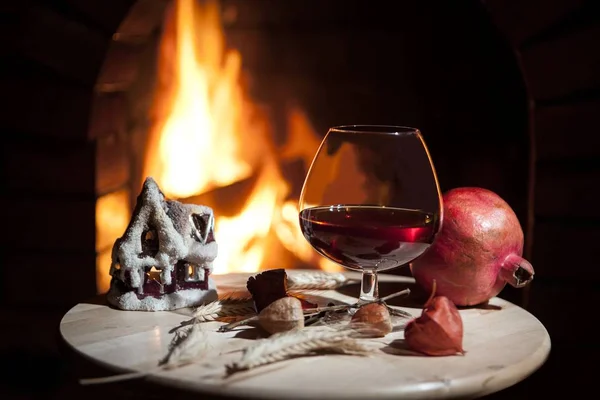 Glass of brandy, candle,pomegranate, burning fireplace — Stock Photo, Image