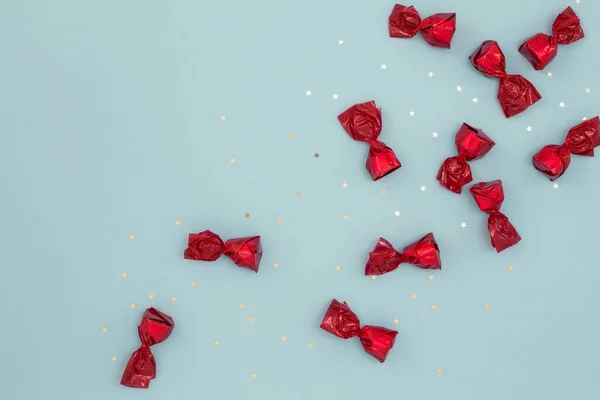 Dulces de chocolate envueltos en papel rojo sobre fondo azul — Foto de Stock