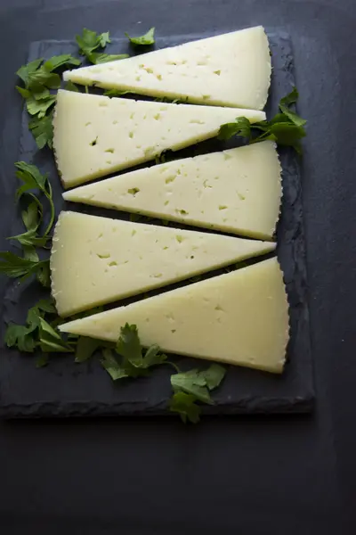 Lots of slices of cheese with parsley on a stone slate — Stock Photo, Image