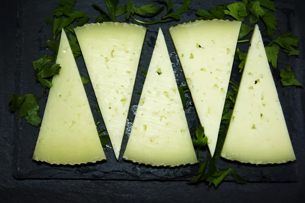 Viele Scheiben Käse mit Petersilie auf einer Steintafel — Stockfoto