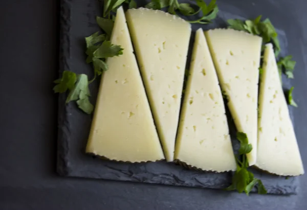 Un sacco di fette di formaggio con prezzemolo su un'ardesia di pietra — Foto Stock