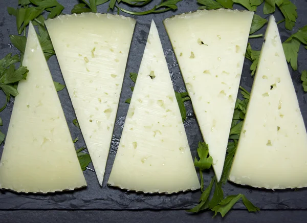 Lots of slices of cheese with parsley on a stone slate — Stock Photo, Image