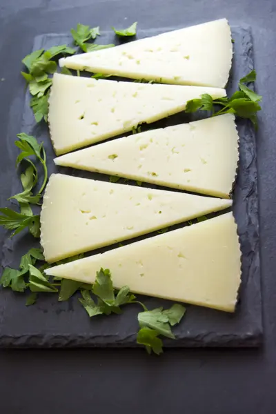 Lots of slices of cheese with parsley on a stone slate — Stock Photo, Image