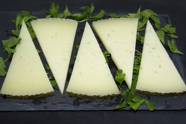 Lots of slices of cheese with parsley on a stone slate — Stock Photo, Image