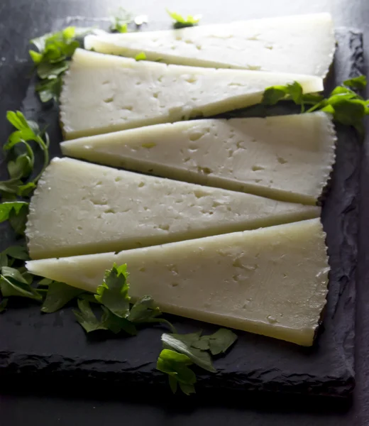 Lots of slices of cheese with parsley on a stone slate — Stock Photo, Image