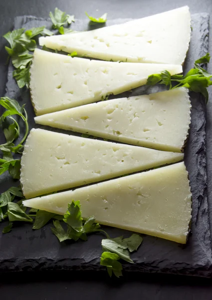 Lots of slices of cheese with parsley on a stone slate — Stock Photo, Image