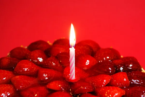 Strawberry cake, almonds and cream with a candle on a red backgr — Stock Photo, Image