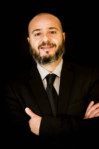 Hombre guapo, calvo con barba, en traje y corbata, sobre fondo negro — Foto de Stock