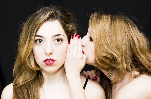 Two beautiful women where one of them is telling a secret to the — Stock Photo, Image