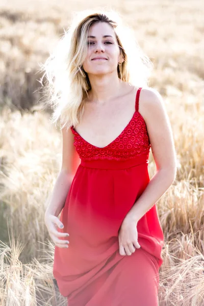 Kırmızı elbiseli, günbatımı buğday sahasının güzel sarışın kadın — Stok fotoğraf