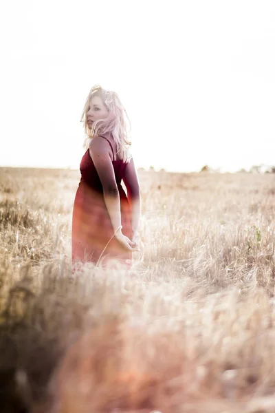 Mooie blonde vrouw in een rode jurk, op een tarweveld bij zonsondergang — Stockfoto