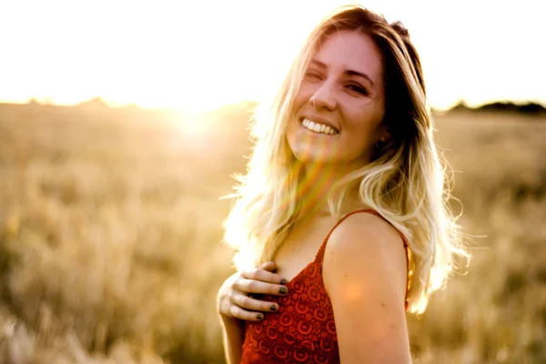 Mulher loira bonita em um vestido vermelho, em um campo de trigo ao pôr do sol — Fotografia de Stock