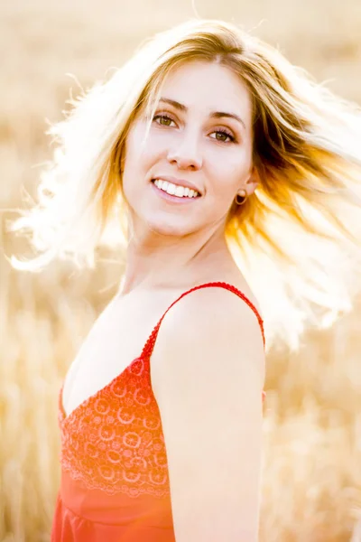 Beautiful blond woman in a red dress, on a wheat field at sunset — Stock Photo, Image