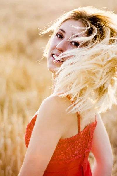 Mulher loira bonita em um vestido vermelho, em um campo de trigo ao pôr do sol — Fotografia de Stock