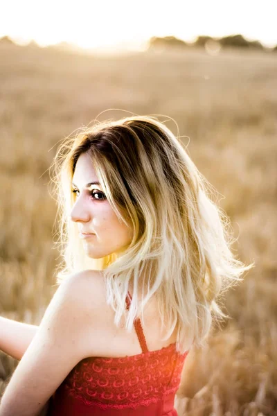 Belle femme blonde en robe rouge, sur un champ de blé au coucher du soleil — Photo