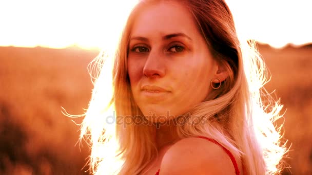 Mulher loira bonita em um vestido vermelho, em um campo de trigo ao pôr do sol — Vídeo de Stock