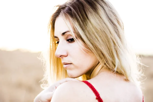 Mooie blonde vrouw in een rode jurk, op een tarweveld bij zonsondergang — Stockfoto