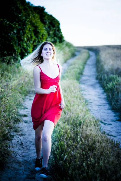 Beautiful blond woman in a red dress on a path in the wheat fiel — Stock Photo, Image