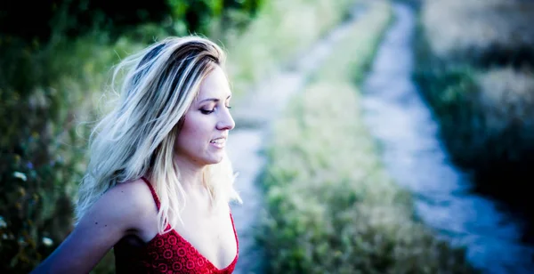 Mooie blonde vrouw in een rode jurk op een pad in de tarwe-fiel — Stockfoto