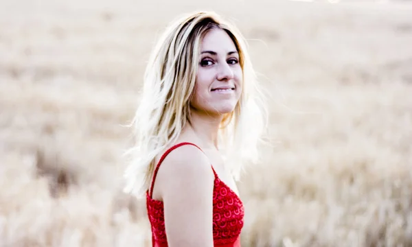 Schöne blonde Frau in einem roten Kleid, auf einem Weizenfeld bei Sonnenuntergang — Stockfoto