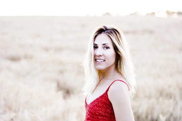 Belle femme blonde en robe rouge, sur un champ de blé au coucher du soleil — Photo