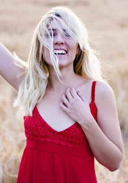 Mooie blonde vrouw in een rode jurk, op een tarweveld bij zonsondergang — Stockfoto