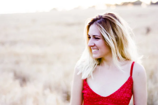 Bella donna bionda in abito rosso, su un campo di grano al tramonto — Foto Stock