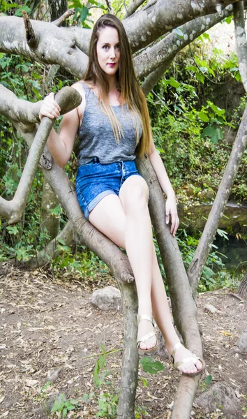 Schöne Frau, die auf einem Ast am Ufer eines Berges sitzt — Stockfoto