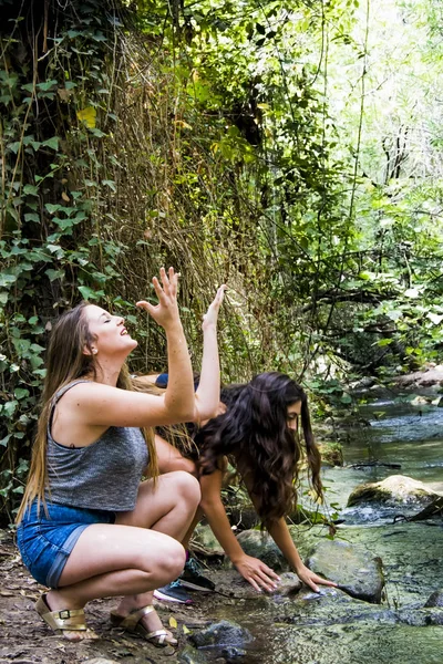 Dos hermosas mujeres en la naturaleza, salpicando agua en un río de un — Foto de Stock