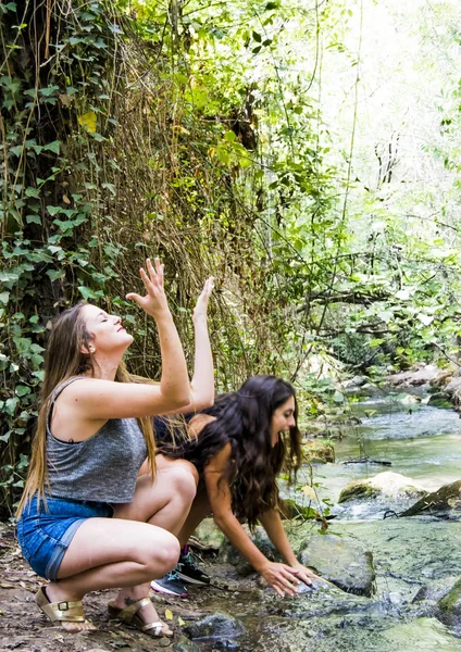 Dos hermosas mujeres en la naturaleza, salpicando agua en un río de un — Foto de Stock