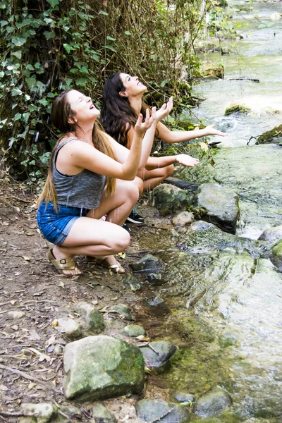 Dos hermosas mujeres en la naturaleza, salpicando agua en un río de un — Foto de Stock