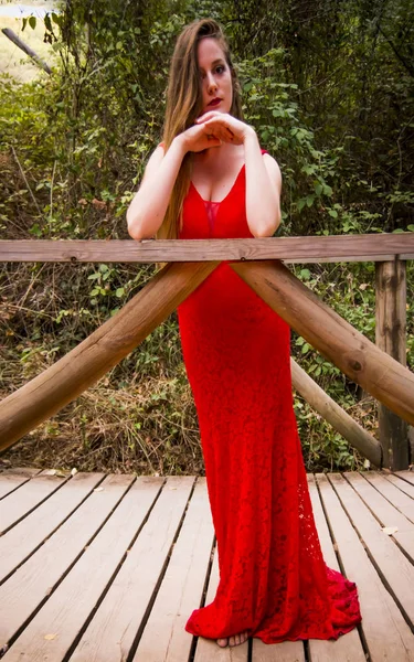 Schöne Frau auf dem Feld auf einer Holzbrücke trägt ein rotes ev — Stockfoto
