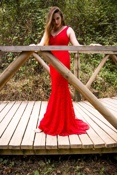 Hermosa mujer en el campo en un puente de madera con un ev rojo — Foto de Stock