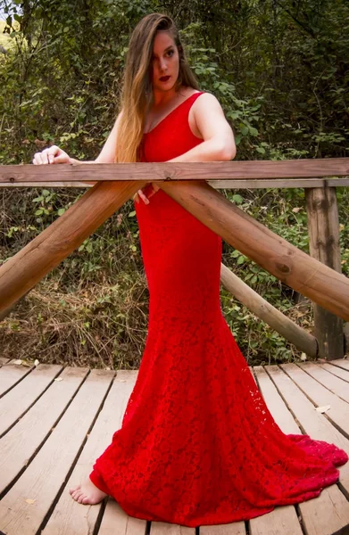 Schöne Frau auf dem Feld auf einer Holzbrücke trägt ein rotes ev — Stockfoto