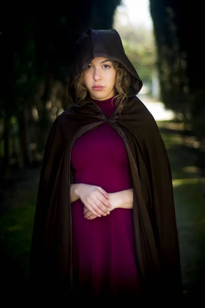 Beautiful woman with cape on a path in the woods