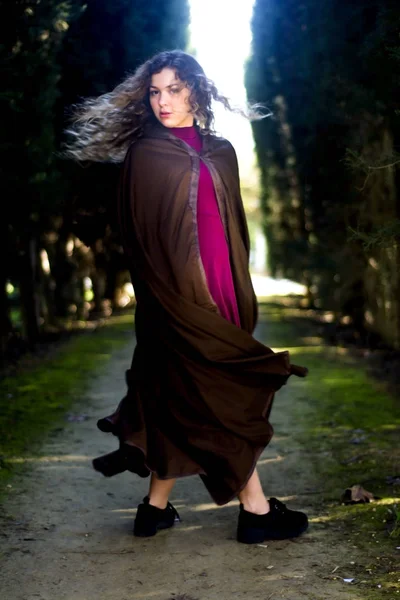 Beautiful woman with cape on a path in the woods