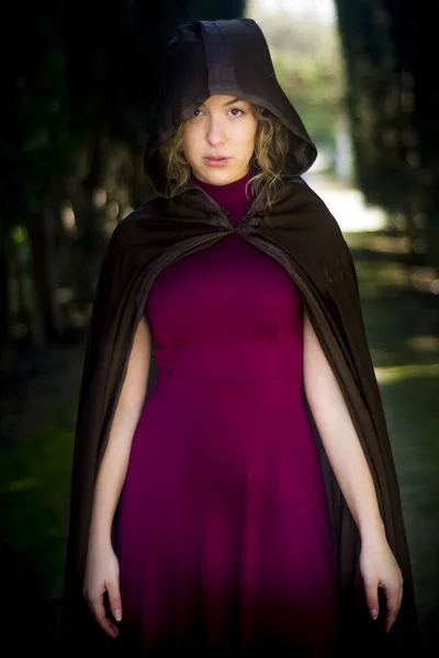 Beautiful woman with cape on a path in the woods