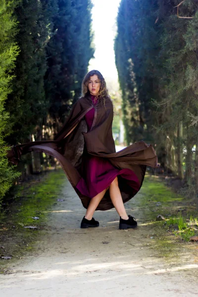 Beautiful woman with cape on a path in the woods